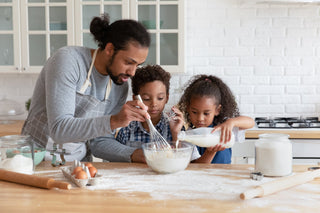 Father and two children mixing flour and milk in a bowl in the kitchen