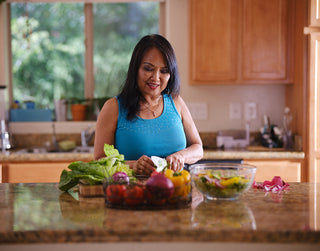 elderly woman in blue shirt cutting up vegetables in her home kitchen
