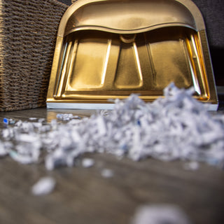 copper colored dust pan with shredded paper in front of it on floor