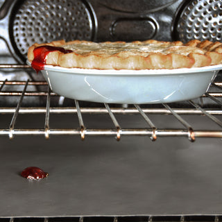 cherry pie in stoneware pie plate in oven with cherry juice running over and landing on the nonstick oven liner