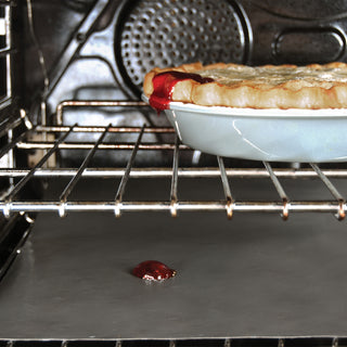 Pie being baked in an oven with a small amount of cherry pie filling bubble over on the nonstick oven liner.