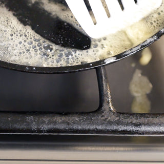 a close up of a pan with ingredients boiling over onto the universal gas stovetop liners to demonstrate how they catch spills during cooking.