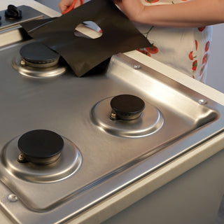 a person trimming the universal gas stove top liner with household scissors to get the proper fit for each burner. 