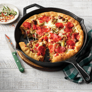Pepperoni pizza in a taste of home preseasoned cast iron skillet on a wooden board with a checkered cloth and small plate of vegetables in the background.