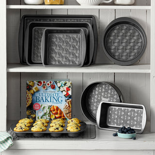 Set of taste of home nonstick metal baking pans and a cookbook on a shelf with a wooden background