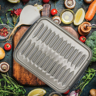 Chrome grill pan surrounded by fresh vegetables on a dark surface