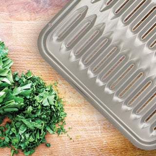 Chrome grill pan on a wooden surface with chopped greens nearby
