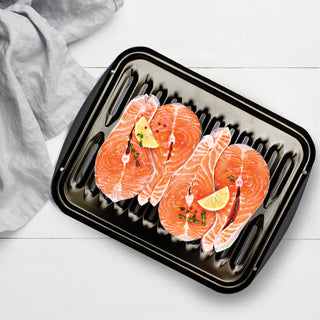 Three raw salmon fillets with lemon wedges on a black broiler pan.