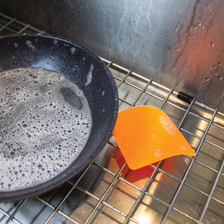 Dish with soapy water and orange scraper on a metal rack