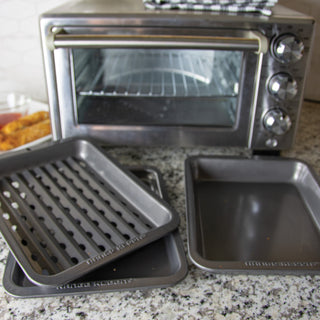 Silver toaster oven with three toaster oven bakeware pieces on a granite countertop