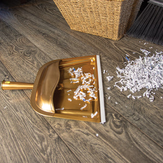 copper colored metal hooded dust pan on gray flooring with shredded paper