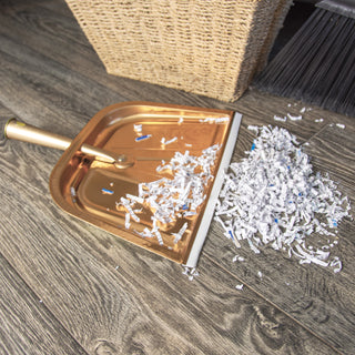 copper colored metal dust pan on gray flooring with shredded paper