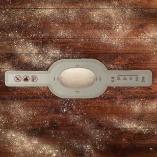 dough ready for final rise on an oval silicone bread sling on a wooden table with flour sprinkled across the tabletop