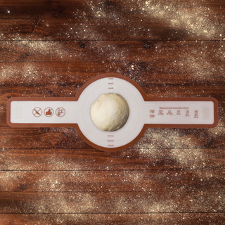 dough in center of flat round silicone bread sling before final rise on wooden table with flour sprinkled on tabletop