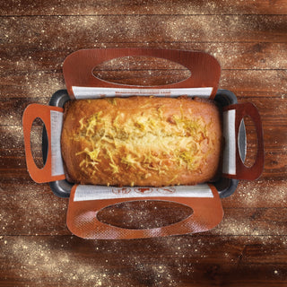 baked lemon bread inside a baking sling in a loaf pan on a wooden table with flour sprinkles