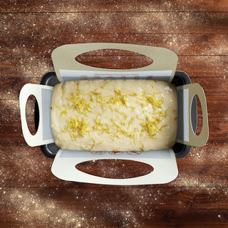 batter inside a baking sling in a loaf pan on a wooden table with flour sprinkles