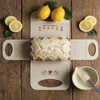 oatmeal silicone baking sling laying flat on wooden table with iced lemon quick bread and accessories