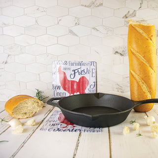 1 farmhouse rooster hot pad under skillet on counter 1 farmhouse rooster propped on back wall with bread beside it.