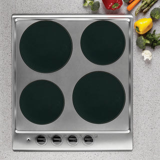 Overhead view of black burner covers on top of stainless steel stove with vegetables on counter.