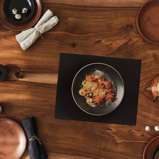 Black matte counter mat used on wooden table top with place settings and hot pasta dish on mat. 