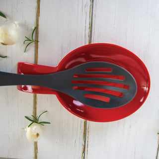 slotted spoon on a red spoon rest on a white wooden surface with garlic and rosemary.