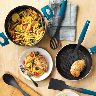 Cookware set with pasta, chicken, and vegetables on a wooden table