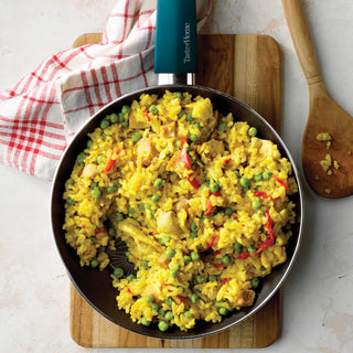 Frying pan with yellow rice and vegetables on a wooden cutting board with a red and white towel.