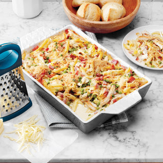 Pasta dish with vegetables and cheese in a baking dish on a marble countertop.
