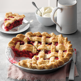 Raspberry pie with a slice taken out, served on a plate with a bowl of whipped cream and a mug.