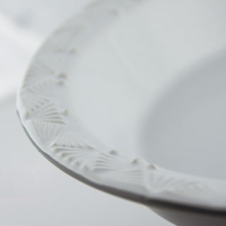 Close-up of a white stoneware plate with subtle patterns on a light gray background