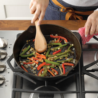 Person cooking vegetables in a Taste of Home Pre-Seasoned Cast Iron Skillet on a stove