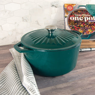 Taste of Home 5-Quart Enameled Cast Iron Dutch Oven w/Self-Basting Lid on a wooden surface with a cookbook in the background.