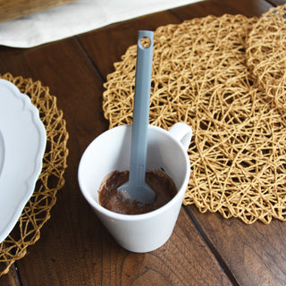 White mug with chocolate content and a Taste of Home Mini Spatula in Ash Gray spoon on a wooden surface with a textured mat.