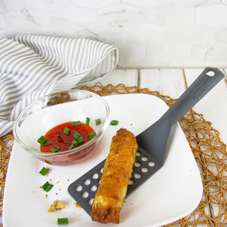 Egg roll on a vented taste of home turner with a side of sauce and green onions on a white plate.