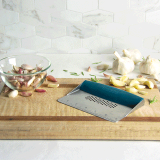 a gif of a taste of home bench scraper showing how to cut and crush garlic