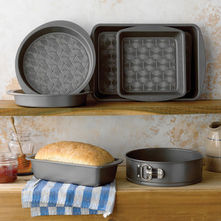 Set of gray baking pans on a wooden shelf with bread and kitchen items.