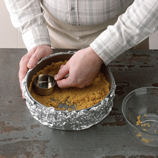 Person preparing a dessert by pressing crumbs into a foil-lined 9-Inch Non-Stick Metal Springform Baking Pan