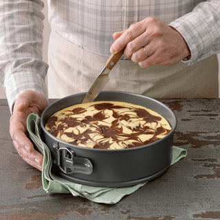 Person removing a marble cake from a 9-Inch Non-Stick Metal Springform Baking pan with a spatula.