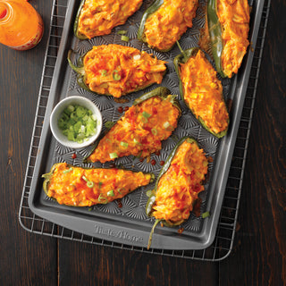 Tray of buffalo-styled stuffed peppers with a small bowl of green onions on a Taste of Home Nonstick metal baking sheet and cooling rack on a dark surface.