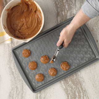 Person scooping cookie dough onto a taste of home baking sheet with a bowl of cookie dough nearby.