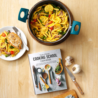 taste of home dutch oven cookware with pasta, plate of chicken and pasta and cooking school cookbook on table